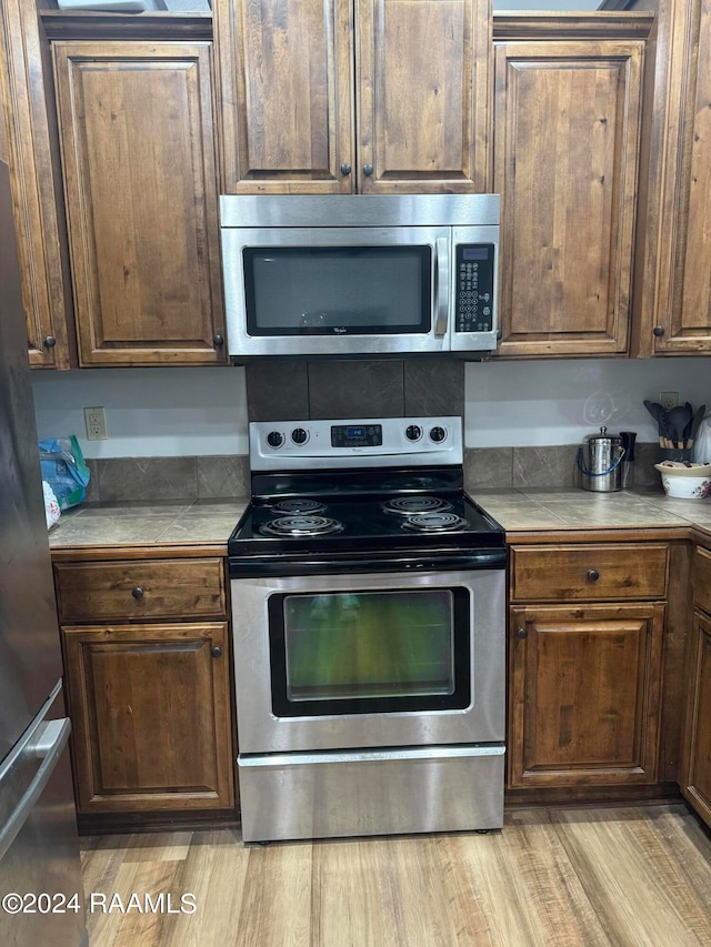 kitchen with light wood-type flooring, appliances with stainless steel finishes, and tile countertops