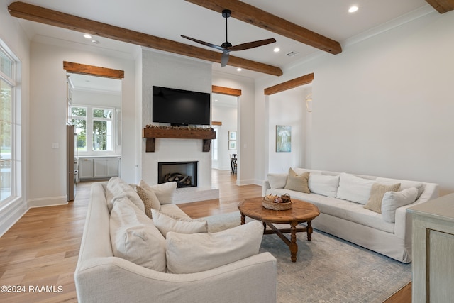 living room featuring a fireplace, beamed ceiling, crown molding, ceiling fan, and light hardwood / wood-style flooring