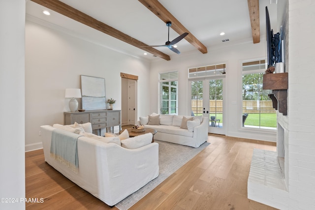 living room with ceiling fan, light wood-type flooring, beam ceiling, and a healthy amount of sunlight