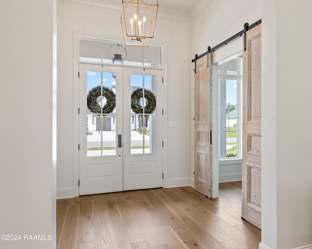 foyer entrance featuring a chandelier, light hardwood / wood-style floors, crown molding, and a barn door