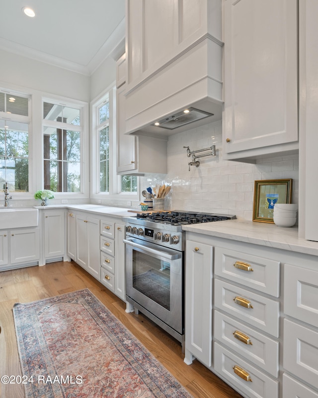 kitchen featuring high end stainless steel range, white cabinets, light hardwood / wood-style flooring, premium range hood, and sink