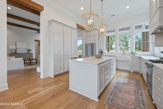 kitchen featuring pendant lighting, beamed ceiling, a kitchen island, stainless steel appliances, and light hardwood / wood-style floors