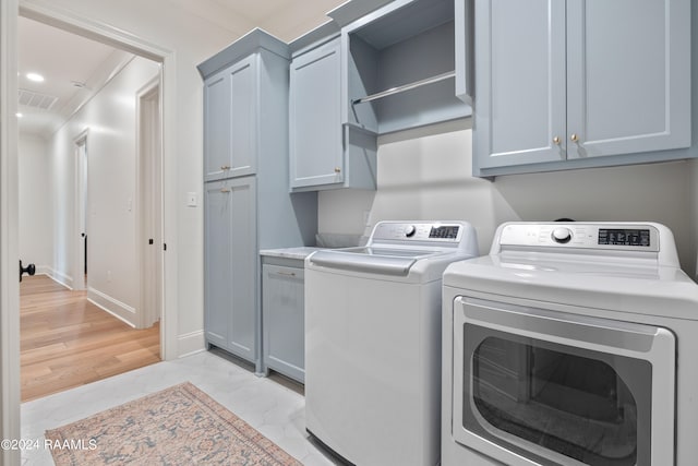 washroom with light wood-type flooring, washer and dryer, and cabinets