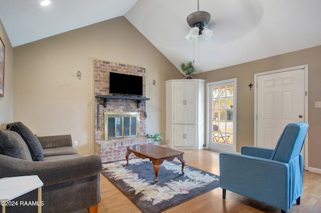 living room with light wood-type flooring, lofted ceiling, ceiling fan, and a brick fireplace