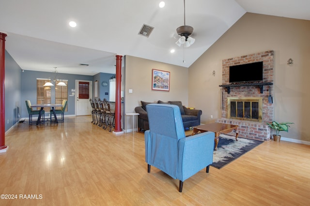 living room with wood-type flooring, a brick fireplace, vaulted ceiling, ceiling fan with notable chandelier, and ornate columns