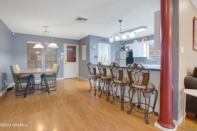 kitchen featuring light hardwood / wood-style floors, white cabinetry, kitchen peninsula, hanging light fixtures, and stainless steel fridge