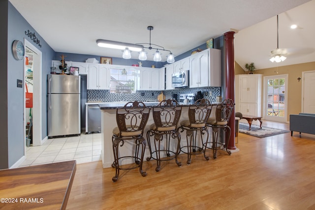 kitchen with kitchen peninsula, white cabinetry, appliances with stainless steel finishes, a breakfast bar area, and light hardwood / wood-style floors