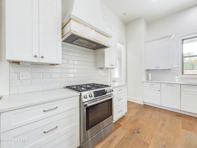 kitchen with custom exhaust hood, backsplash, white cabinetry, stainless steel stove, and light wood-type flooring