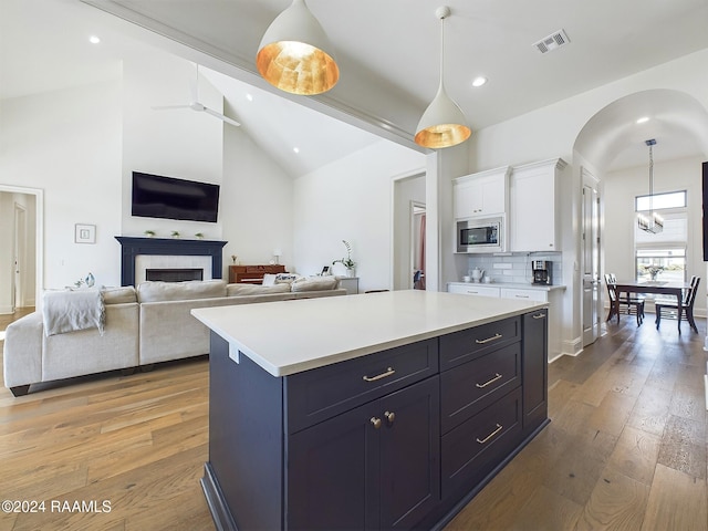 kitchen featuring white cabinets, hanging light fixtures, stainless steel microwave, light hardwood / wood-style flooring, and a center island