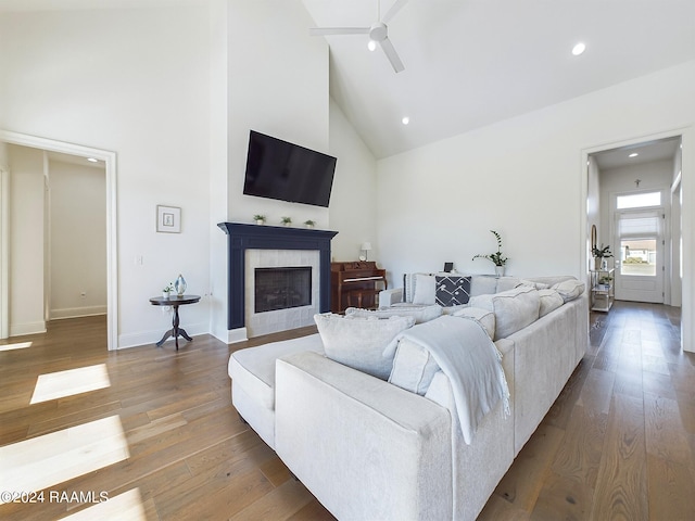 living room featuring ceiling fan, high vaulted ceiling, a tile fireplace, and hardwood / wood-style floors