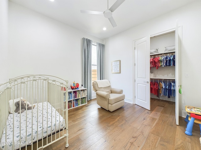 bedroom with a closet, ceiling fan, hardwood / wood-style flooring, and a nursery area