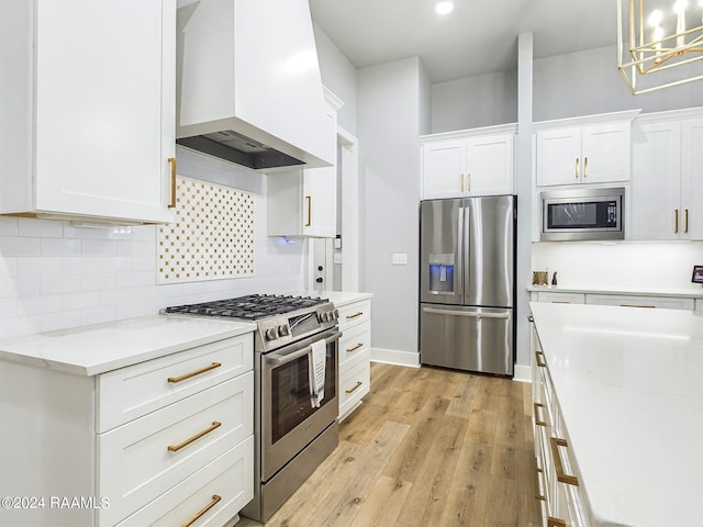 kitchen with custom range hood, white cabinets, pendant lighting, appliances with stainless steel finishes, and light hardwood / wood-style floors