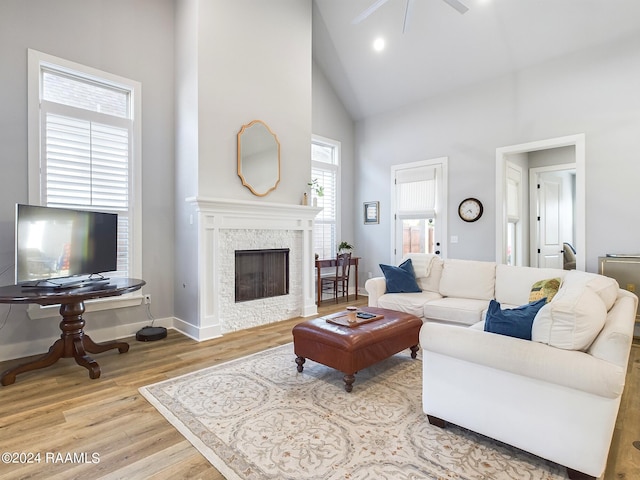 living room with a stone fireplace, high vaulted ceiling, light wood-type flooring, and ceiling fan