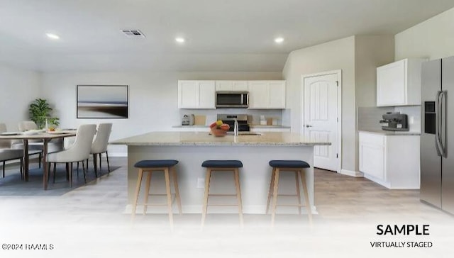 kitchen featuring light stone countertops, an island with sink, appliances with stainless steel finishes, a kitchen bar, and white cabinetry