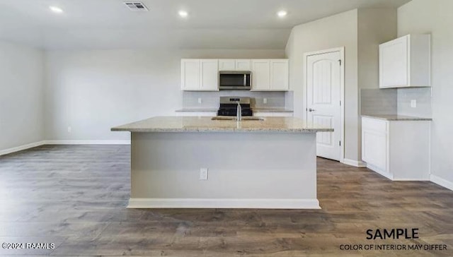 kitchen with dark wood-type flooring, white cabinets, a center island with sink, light stone counters, and stainless steel appliances