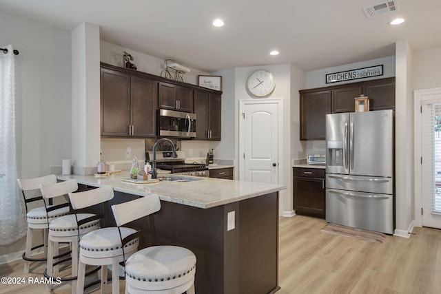 kitchen with kitchen peninsula, light hardwood / wood-style flooring, appliances with stainless steel finishes, dark brown cabinets, and a kitchen breakfast bar