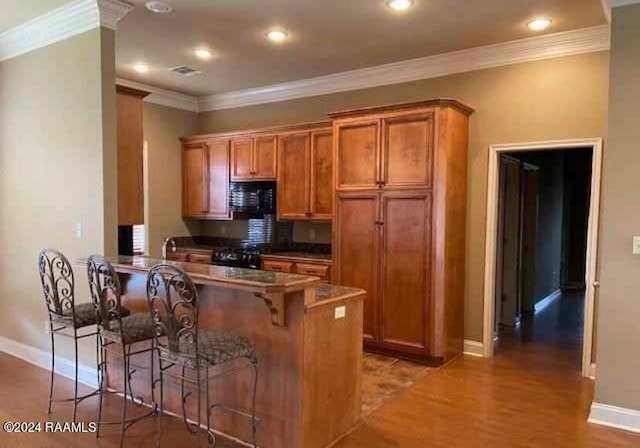 kitchen featuring a breakfast bar, hardwood / wood-style flooring, kitchen peninsula, black appliances, and crown molding