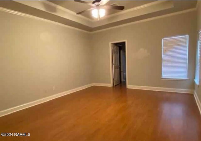 unfurnished room featuring ceiling fan, a raised ceiling, crown molding, and dark hardwood / wood-style flooring