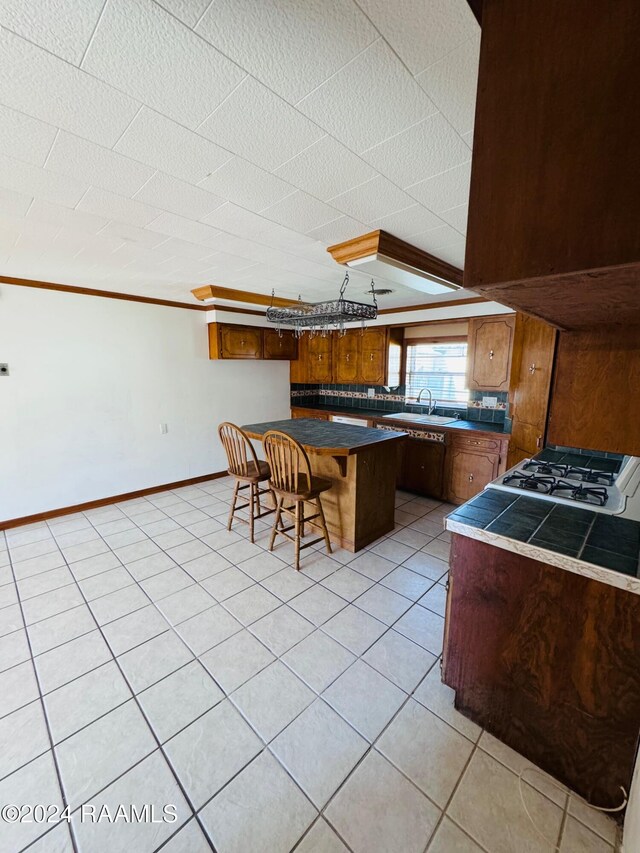 205 Gauraud St, Abbeville, LA 70510 - kitchen featuring cooktop, light tile patterned floors, a breakfast bar, a sink, and brown cabinetry