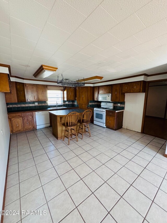 205 Gauraud St, Abbeville, LA 70510 - kitchen with white appliances, dark countertops, a sink, a kitchen bar, and light tile patterned floors