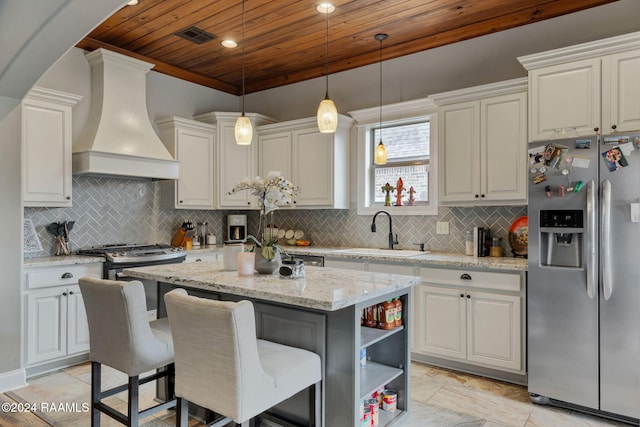 kitchen featuring light stone counters, sink, custom exhaust hood, a kitchen island, and stainless steel fridge