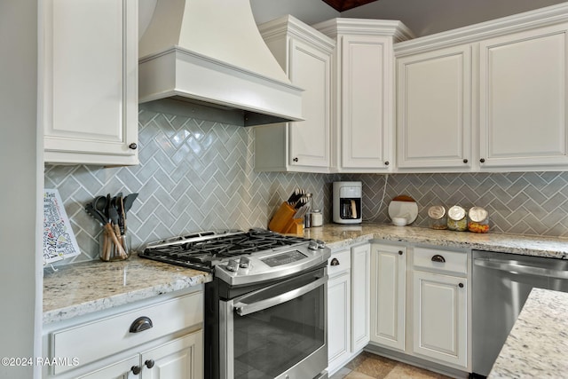 kitchen featuring stainless steel appliances, custom range hood, white cabinets, and backsplash