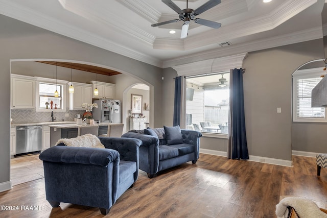 living room with ceiling fan, a tray ceiling, hardwood / wood-style flooring, and ornamental molding