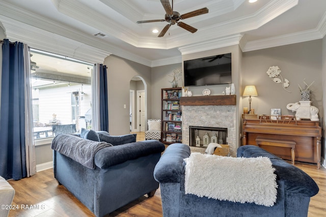 living room featuring a stone fireplace, light hardwood / wood-style flooring, crown molding, and a tray ceiling