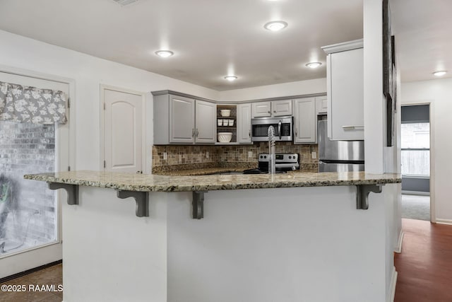 kitchen with appliances with stainless steel finishes, a kitchen bar, dark stone counters, and gray cabinetry