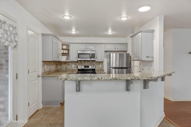 kitchen with a kitchen bar, light stone counters, tasteful backsplash, kitchen peninsula, and stainless steel appliances