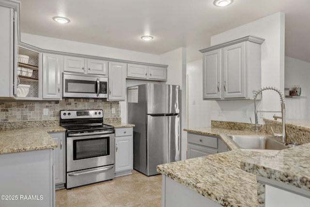 kitchen featuring tasteful backsplash, stainless steel appliances, light stone countertops, and sink