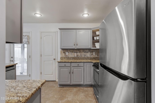 kitchen with gray cabinets, appliances with stainless steel finishes, light stone counters, and decorative backsplash