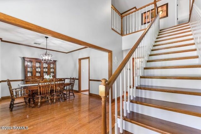 stairway featuring ornamental molding, a notable chandelier, and wood-type flooring