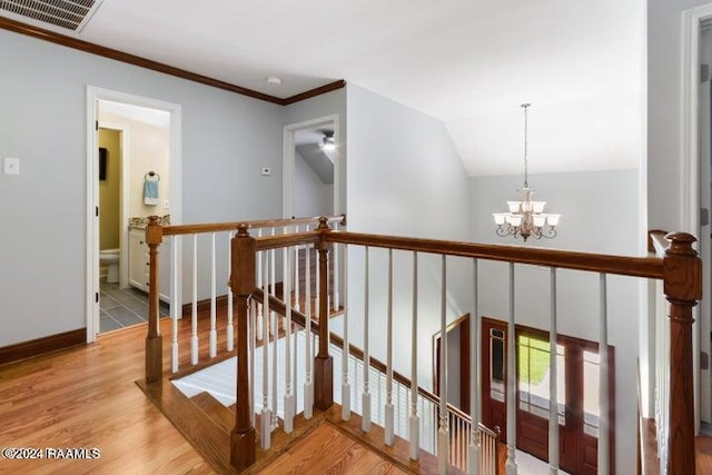 hallway featuring lofted ceiling, ornamental molding, a chandelier, and light hardwood / wood-style flooring