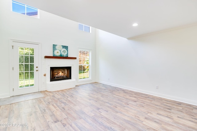 unfurnished living room featuring light hardwood / wood-style floors, a fireplace, and a high ceiling