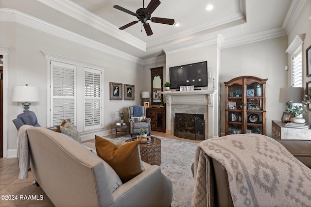 living room featuring a tray ceiling, a high end fireplace, crown molding, light tile patterned flooring, and ceiling fan