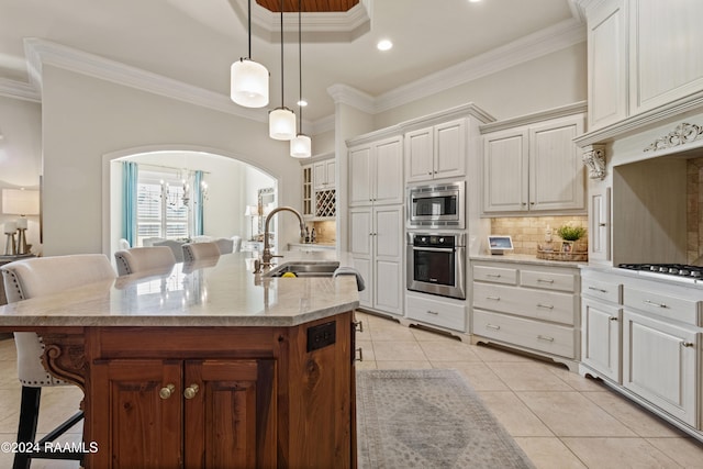 kitchen with a breakfast bar area, crown molding, appliances with stainless steel finishes, and a kitchen island with sink