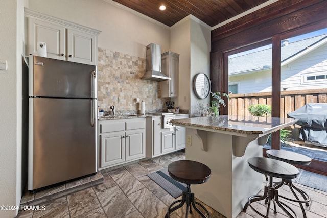 kitchen featuring white cabinets, appliances with stainless steel finishes, wooden ceiling, a kitchen bar, and wall chimney exhaust hood