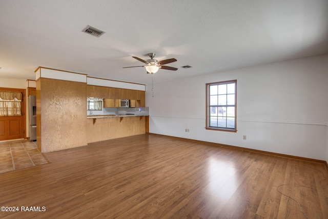 unfurnished living room with a textured ceiling, light wood-type flooring, and ceiling fan