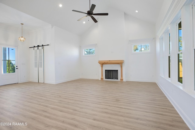 unfurnished living room with ceiling fan, a barn door, high vaulted ceiling, and light hardwood / wood-style flooring