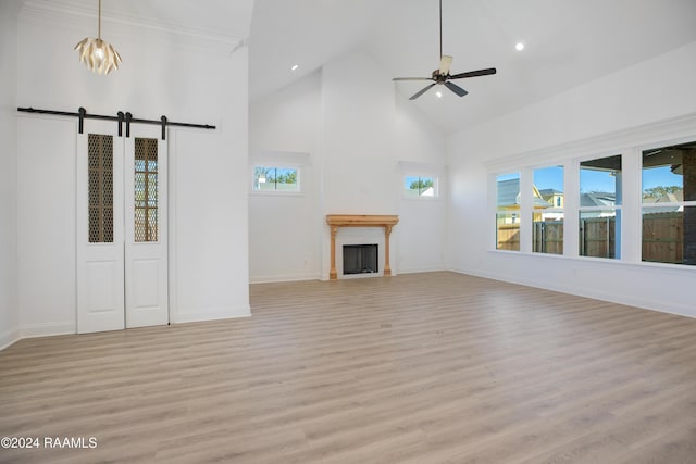 unfurnished living room with a towering ceiling, a barn door, ceiling fan, and light wood-type flooring