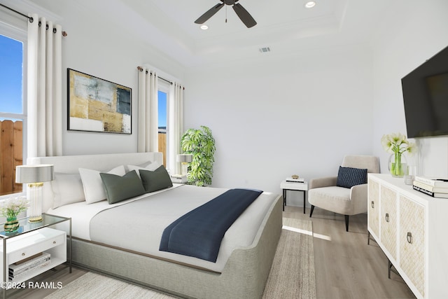 bedroom featuring a raised ceiling, crown molding, ceiling fan, and light hardwood / wood-style flooring