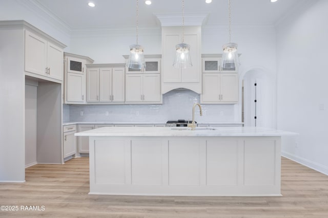 kitchen with sink, decorative light fixtures, ornamental molding, a kitchen island with sink, and white cabinets