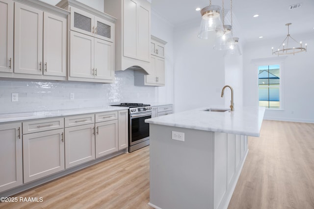 kitchen featuring hanging light fixtures, gas stove, sink, and a center island with sink