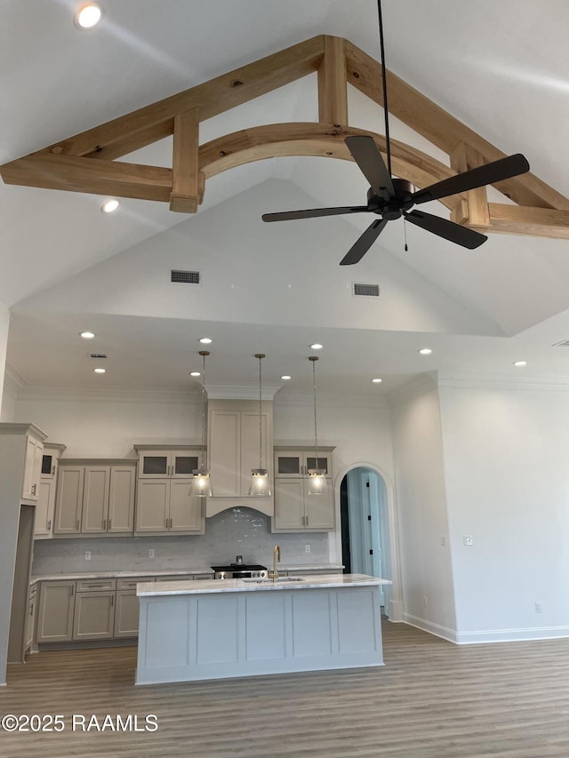 kitchen with gray cabinetry, tasteful backsplash, vaulted ceiling, hanging light fixtures, and a kitchen island with sink