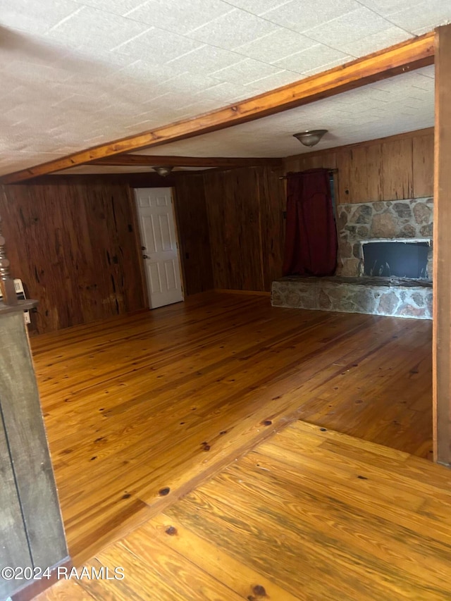 unfurnished living room with hardwood / wood-style flooring, wooden walls, and a stone fireplace