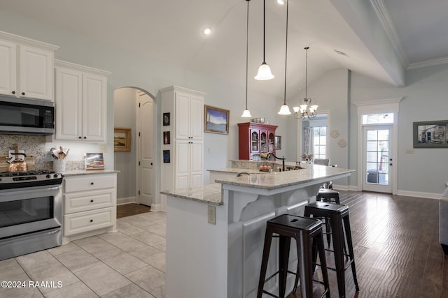 kitchen with appliances with stainless steel finishes, vaulted ceiling, a center island with sink, light hardwood / wood-style flooring, and white cabinetry