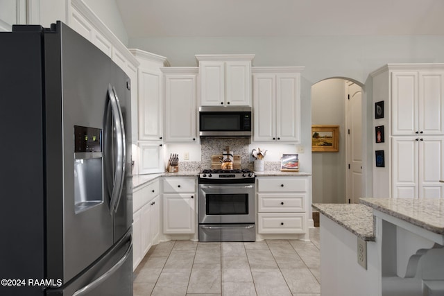 kitchen featuring backsplash, white cabinets, light tile patterned flooring, light stone counters, and stainless steel appliances