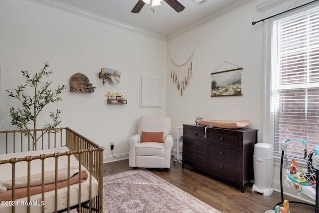 bedroom featuring a crib, crown molding, ceiling fan, and dark wood-type flooring