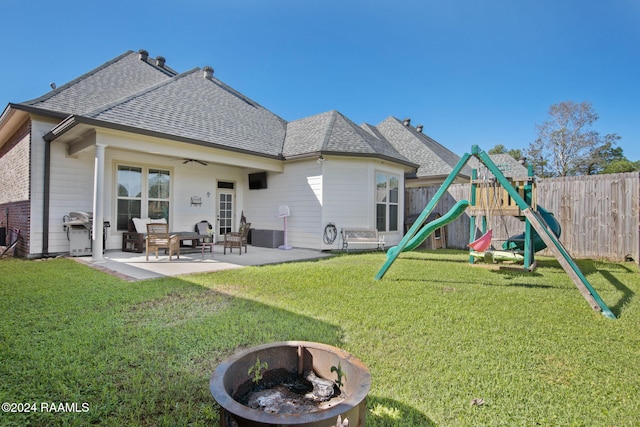 rear view of property featuring a playground, a lawn, a patio, and an outdoor fire pit